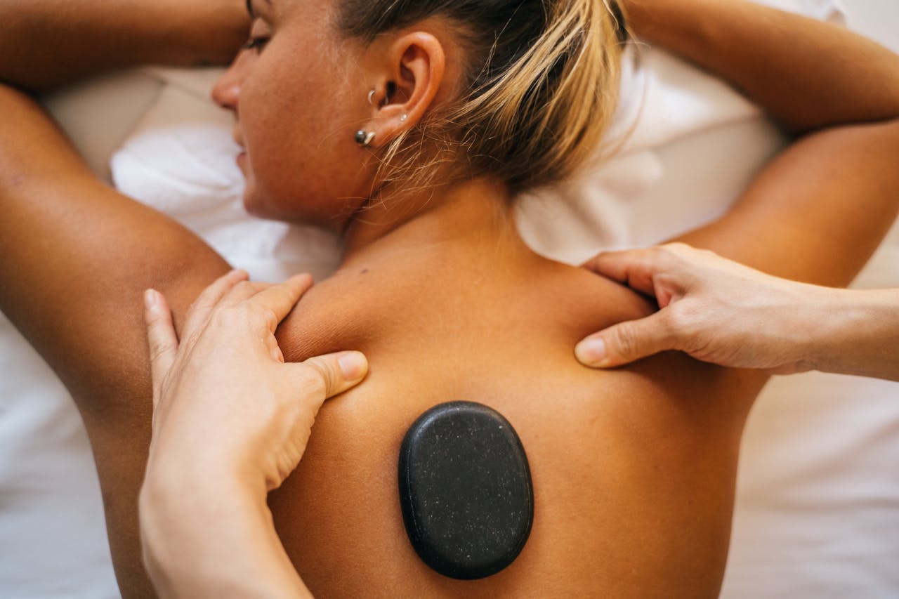Woman receiving a hot stone massage at a spa, promoting relaxation and wellness.